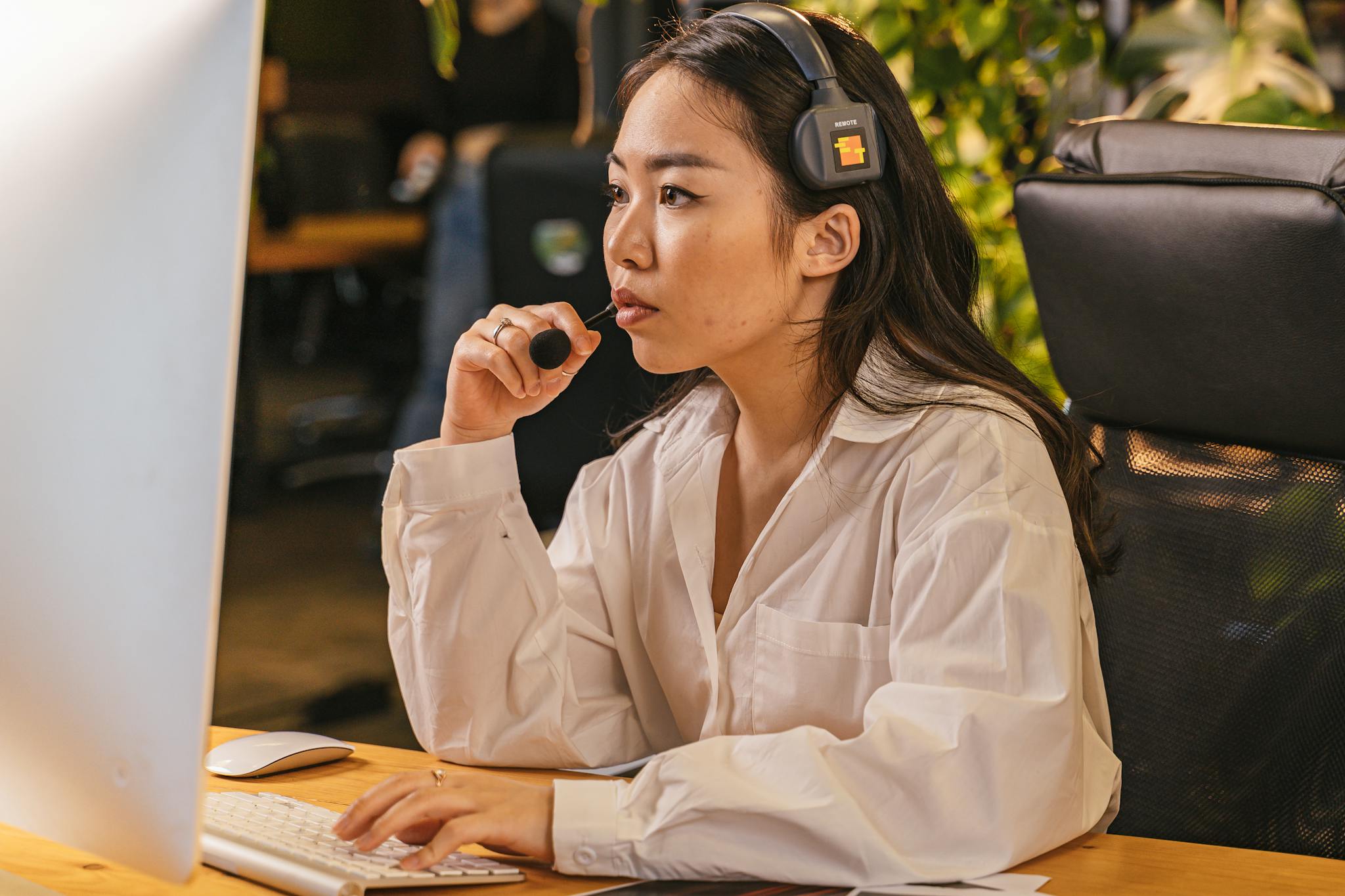 Asian woman working in office, wearing headset, using computer. Business environment with focus and concentration.